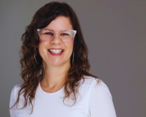 Smiling woman with long brown hair, glasses, and white top