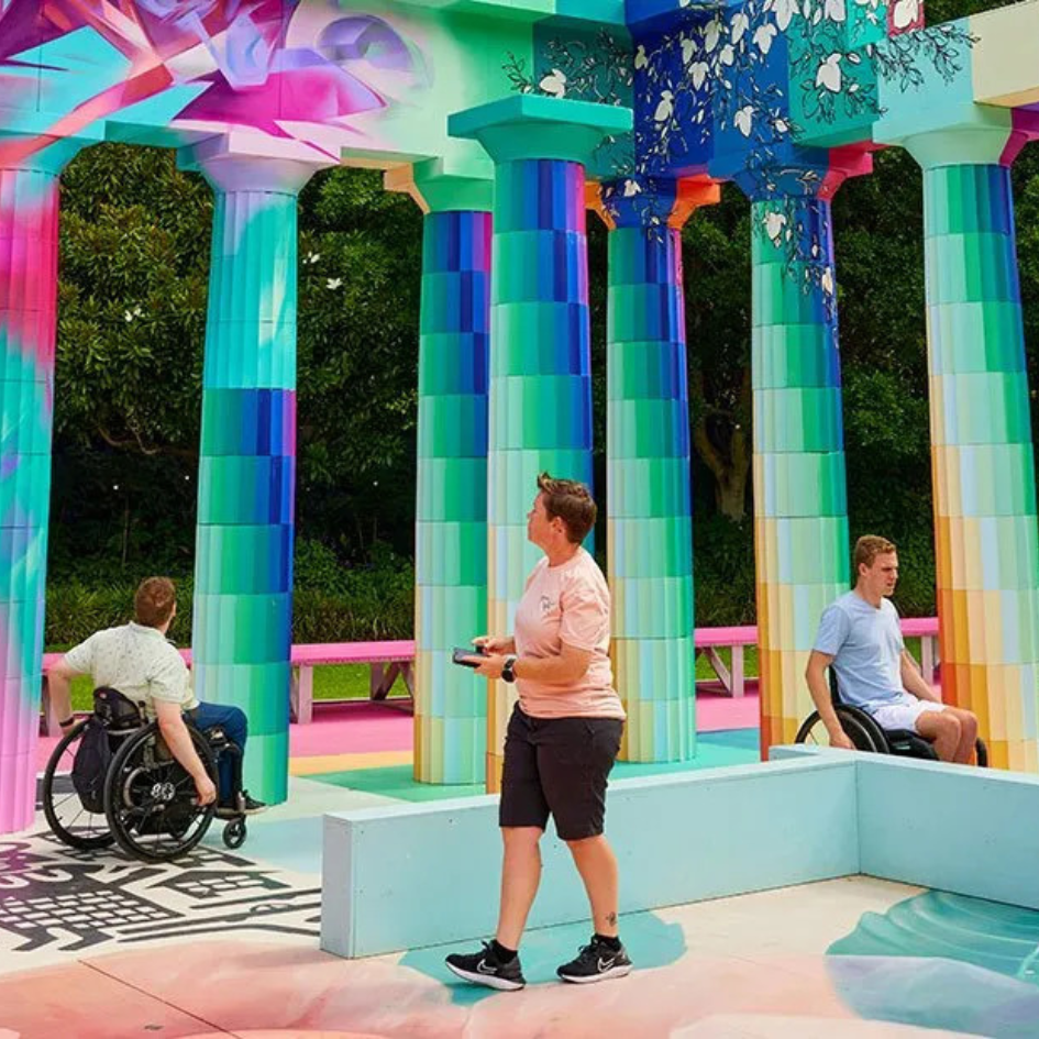 Brightly coloured outdoor temple with people in wheelchairs going past the columns