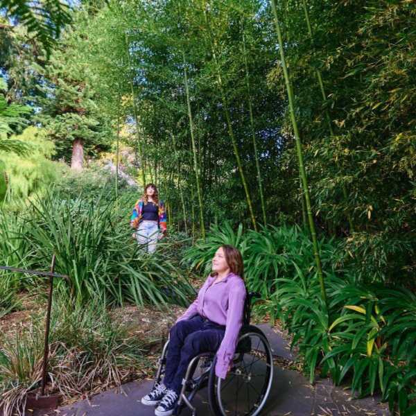 Girl with brown hair in wheelchair with purple shirt and blue pants in a garden