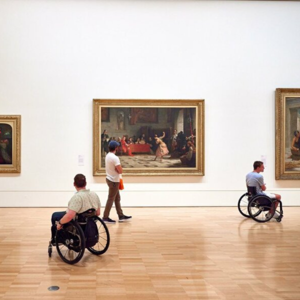 People looking at paintings in an art gallery with two of them in wheelchairs